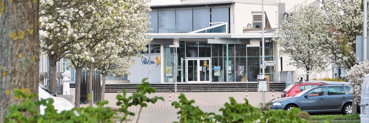 Das Palatinum Mutterstadt Blick durch grüne Bäume auf den Haupteingang des Palatinum Mutterstadt