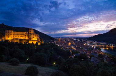 Eine Abbildung des Heidelberger Schlosses bei Nacht über der beleuchteten Stadt