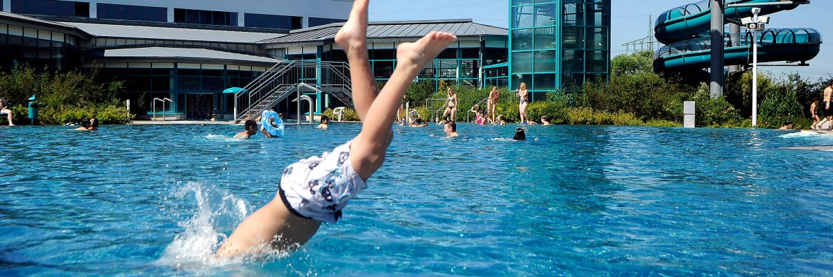 Badende Menschen und ein Junge, der kopfüber ins kühle Nass springt